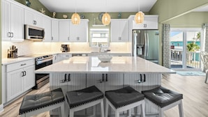 A modern kitchen with white cabinetry, a central island with bar stools, a microwave, stove, and refrigerator. - 🏖️Nirvana in Navarre | Stunning 3BR Home w/ Private Pool + Walk to Beach🏖️ (Navarre)