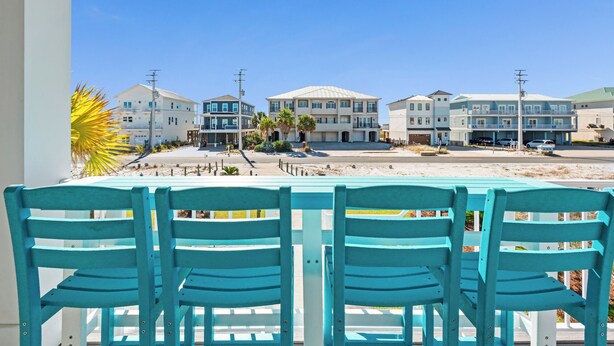 A view of a beachfront property with multiple buildings, a sandy beach, and a row of turquoise chairs. - 🏖️Nirvana in Navarre | Stunning 3BR Home w/ Private Pool + Walk to Beach🏖️ (Navarre)