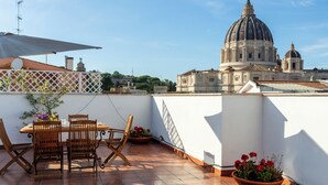 A rooftop terrace with a dining table and chairs, potted plants, and a view of a large dome building. - Saint Peter's Luxury Terrace Suites (Roma)