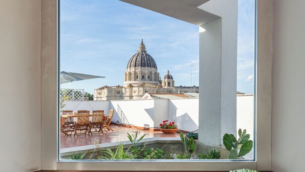 A view from a window overlooking a building with a dome, a patio with chairs and a table, and some plants. - Saint Peter's Luxury Terrace Suites (Roma)
