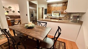 A dining area with a wooden table and chairs, a kitchen with wooden cabinets, and a refrigerator. - Nordic Retreat with private Finnish Sauna (Anchorage)