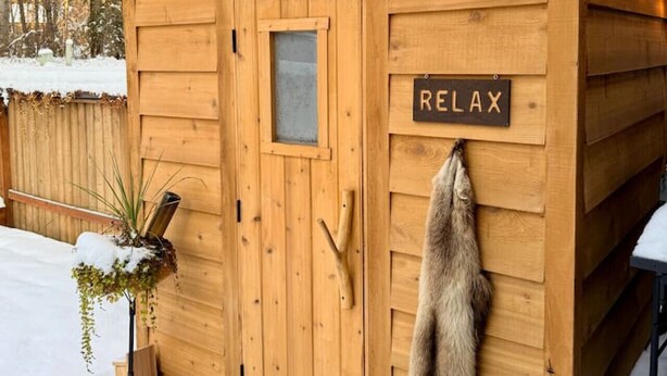 A wooden cabin with a 'RELAX' sign, a fur hanging on the door, and string lights. - Nordic Retreat with private Finnish Sauna (Anchorage)
