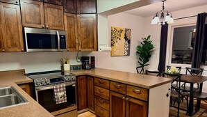 A kitchen with wooden cabinets, a stainless steel microwave, an oven, and a coffee maker. - Nordic Retreat with private Finnish Sauna (Anchorage)