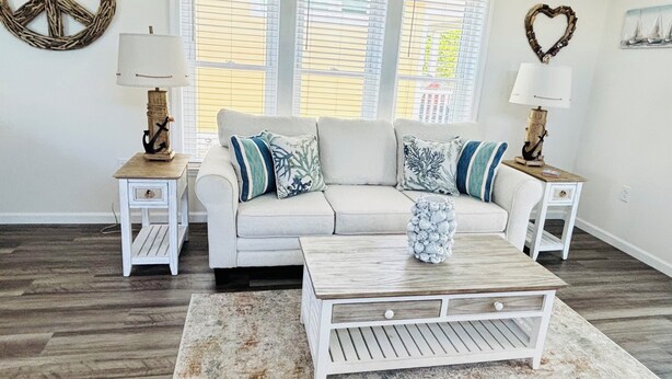 A living room with a white sofa, two side tables with lamps, a coffee table, and a large window with blinds. - Jensen Jewel:  
Clean, new, one bedroom in the beautiful Ocean View community (Jensen Beach)