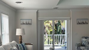 A living room with a sofa, a coffee table, and a patterned armchair. There is a door leading to an outdoor area with a view of greenery and a railing. - Jensen Jewel:  
Clean, new, one bedroom in the beautiful Ocean View community (Jensen Beach)