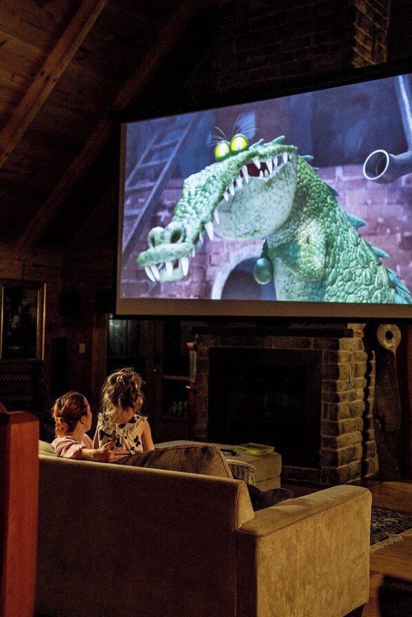 A cozy room with a fireplace, a large screen displaying a movie, and two people watching.