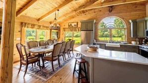 A wooden cabin interior with a dining area, kitchen, and large windows offering a view of the outdoors.
