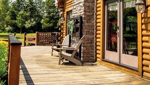 A log cabin with a stone chimney, large windows, and a wooden deck with outdoor seating.
