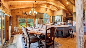 A rustic wooden interior with a dining area, kitchen, and large windows.