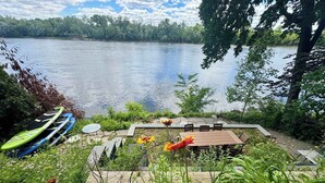 Un patio junto al lago con una mesa y sillas, rodeado de vegetación y vistas al lago.