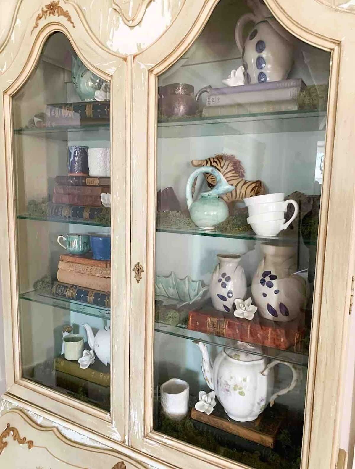 Un meuble vitré avec des étagères contenant divers objets en céramique et des livres.
