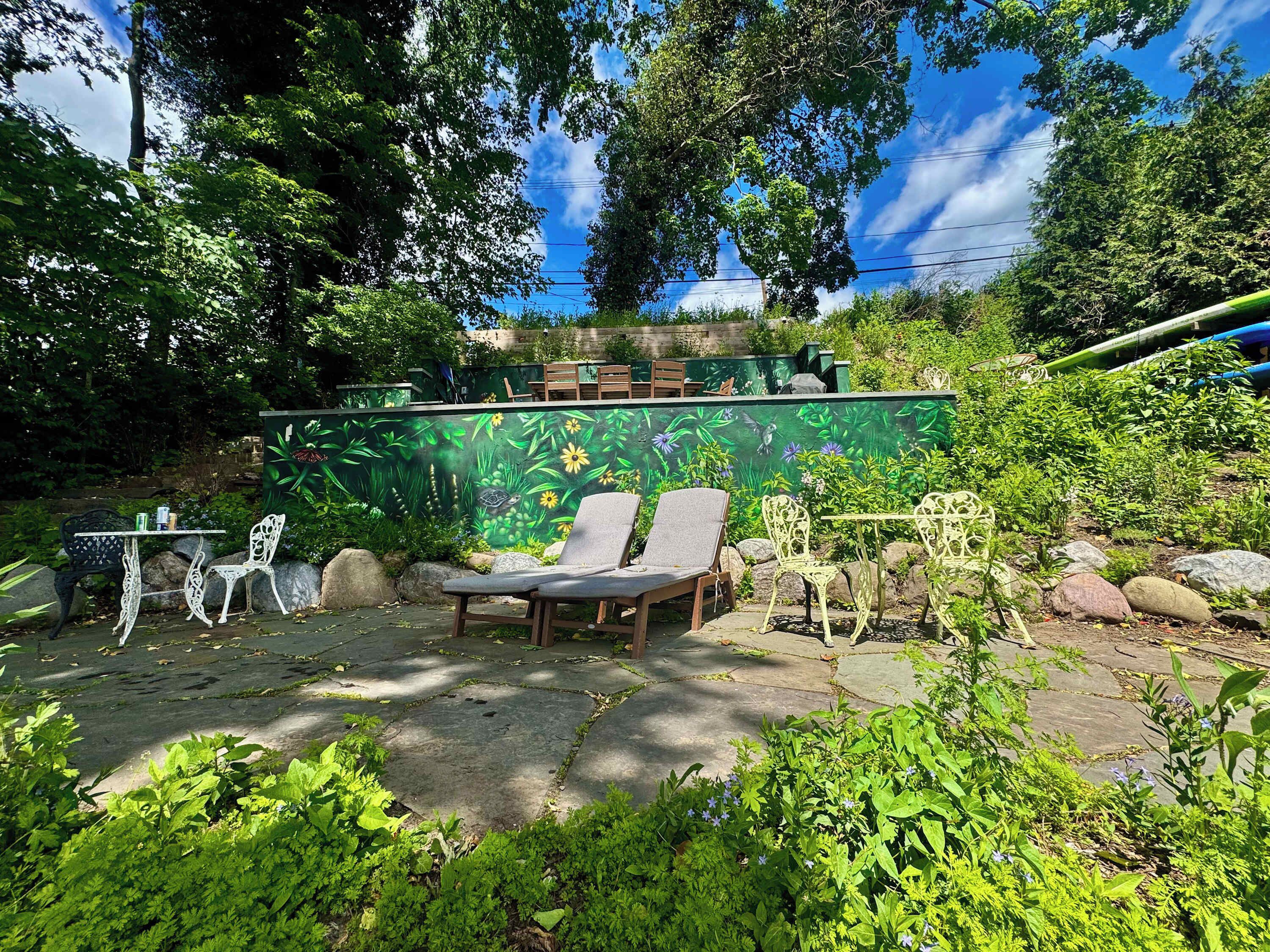 A garden patio with outdoor seating, a mural, and surrounding greenery.
