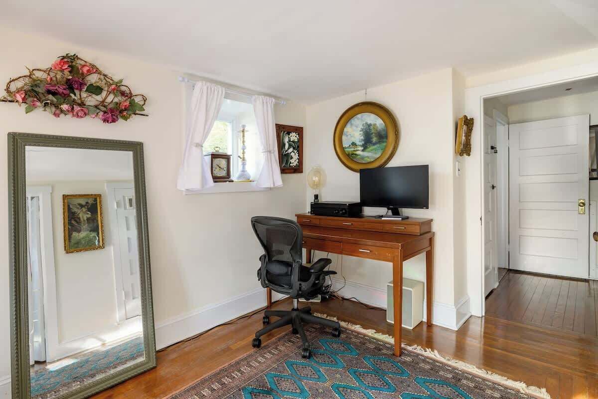 A room with a wooden desk, a computer, a chair, a mirror, a clock, and a door.