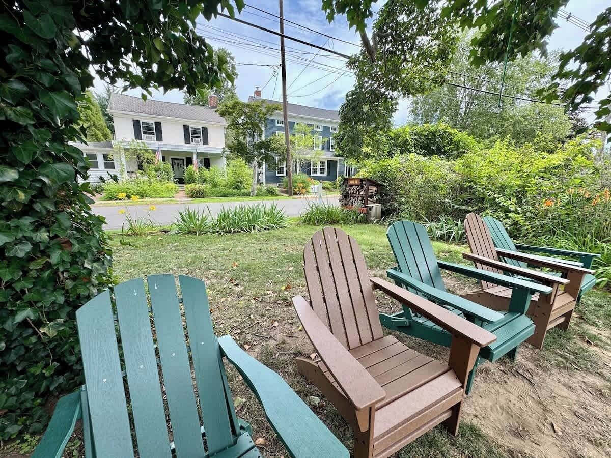 A garden with Adirondack chairs and a house in the background.