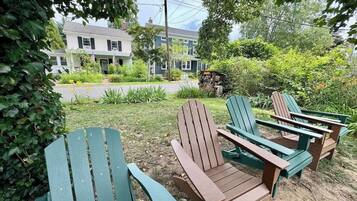 A garden with Adirondack chairs and a house in the background.