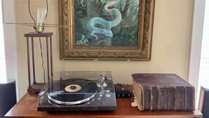 A vintage turntable on a wooden table, a framed painting of a blue bird on the wall, and a stack of old books. - Unique Luxury Central Historic Landmark Home (Lambertville)
