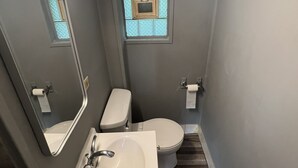 A compact bathroom with a white sink, a toilet, and a small window with a decorative frame. - By The Way Motel Lake Bluff (Lake Bluff)