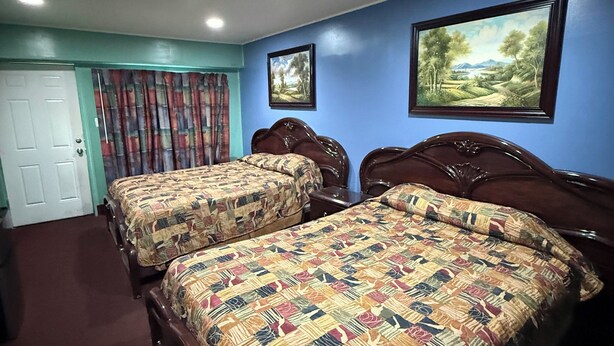 A hotel room with two wooden beds, a door, a curtain, and two framed pictures on the wall. - By The Way Motel Lake Bluff (Lake Bluff)