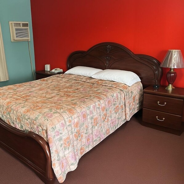 Un dormitorio con una cama de madera, una mesita de noche, una lámpara y una pared roja.