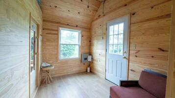 A wooden cabin interior with two windows, a door, a small table, and a bench.