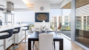 Una cocina moderna con una isla grande, un comedor con una mesa lista para cuatro personas, y vista de la ciudad a través de ventanas amplias.