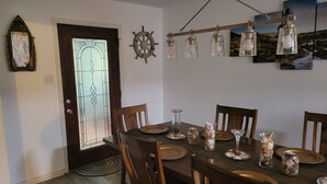 En matplats med ett träbord som är dukat för sex personer, omgivet av trästolar. Ett dekorativt skeppsrat hänger på väggen, och en kristallkrona med klara glödlampor hänger ovanför bordet.