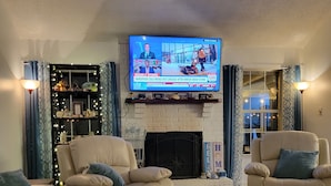 Ett vardagsrum med en öppen spis, två soffor, ett soffbord och en platt-TV som är monterad ovanför spisen.
