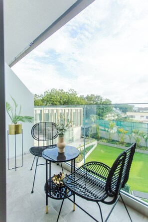 Un balcon doté d’une balustrade en verre, deux chaises en métal noir, une petite table ronde et un pot de fleurs.