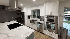 A modern kitchen with white cabinetry, stainless steel appliances, and a marble island. - Casa Del Mar Waterfront Home On Dawon Canal!
Boat Lift and Hot Tub (Saint James City)