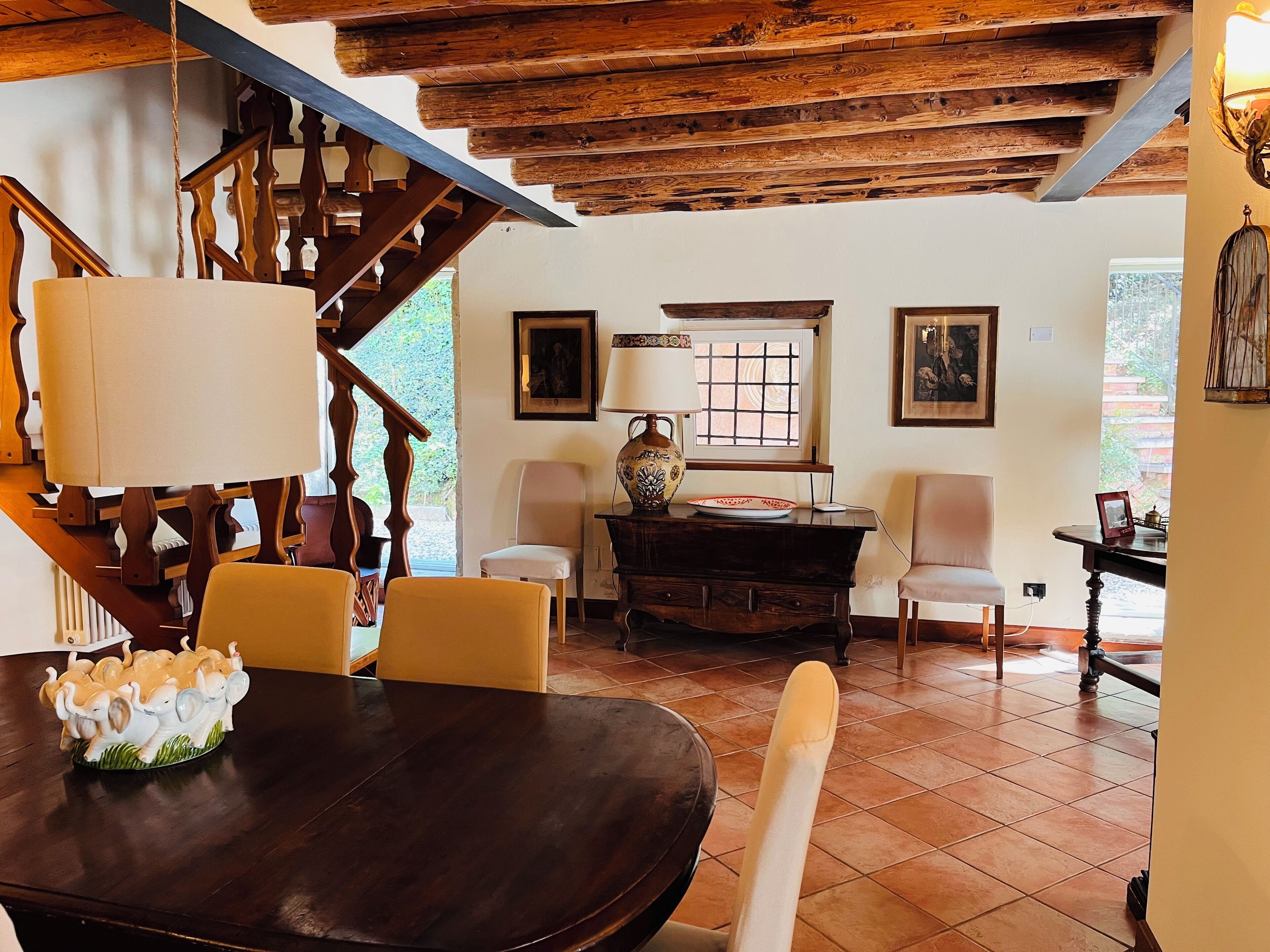 Zona pranzo con tavolo in legno, sedie, una statuina decorativa a forma di elefante, una lampada e una finestra vista verde.