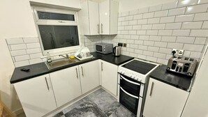 A compact kitchen with white cabinets, a black countertop, a microwave, a stove, and a toaster. - Modern 2 Bed Flat - Ideal for Families  (Ashton-under-Lyne)