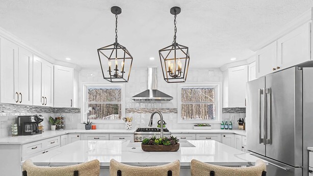 Une cuisine moderne avec des meubles blancs, un grand îlot central doté de tabourets, des appareils en acier inoxydable et un lustre de style rustique.