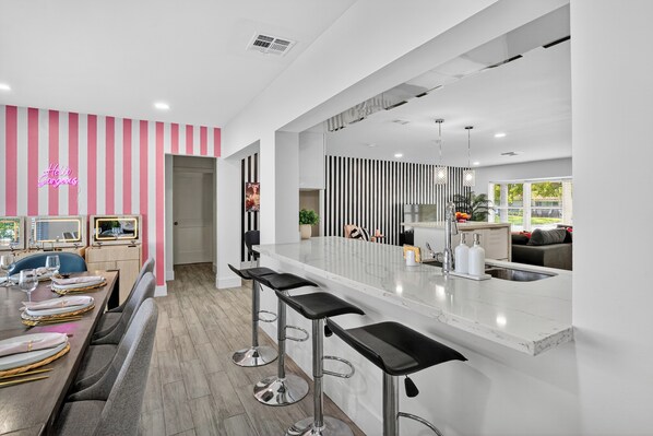 Eine moderne Küche mit einer zentralen Kochinsel, Barhocker und einem Essbereich mit einer Wand in Rosa-Streifen.