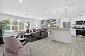 Ein modernes Wohnzimmer mit grauem Sofa, einem runden Couchtisch und einem pinken Sessel.