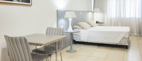 A hotel room with a bed, a desk, a chair, a lamp, and a framed picture on the wall.