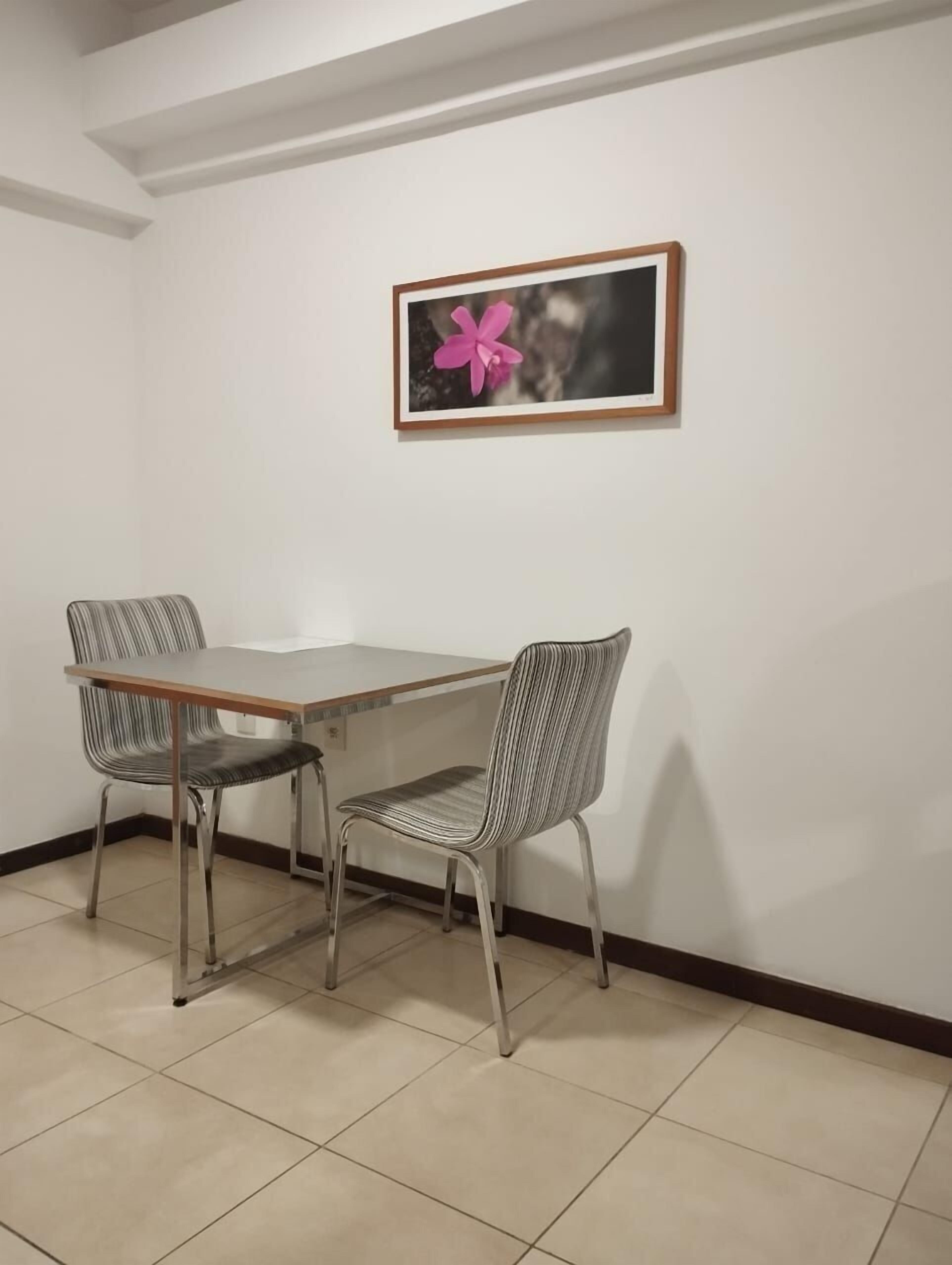 A dining area with a table and two chairs, a framed picture on the wall, and a tiled floor.