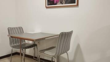 A dining area with a table and two chairs, a framed picture on the wall, and a tiled floor.