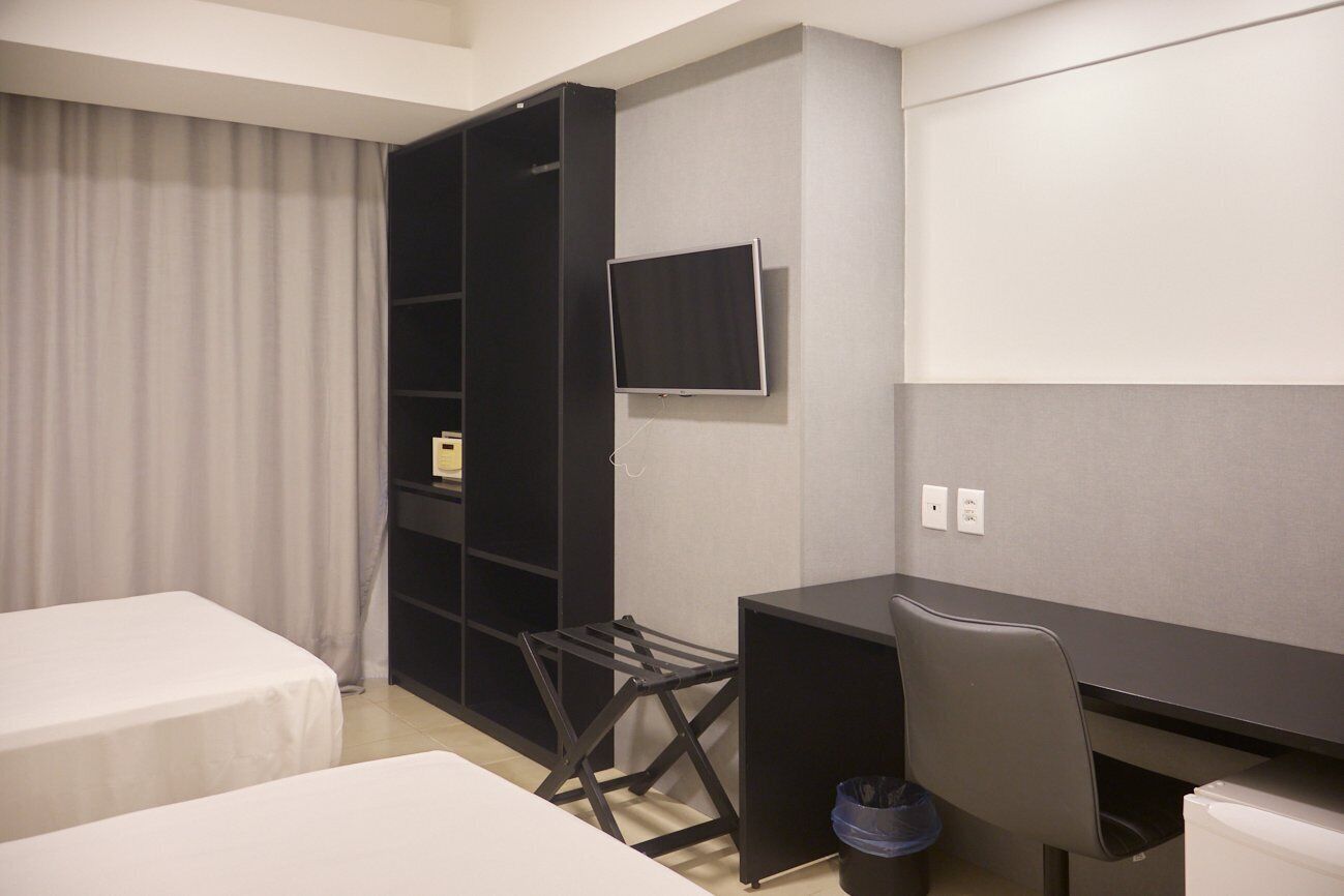 A hotel room with two beds, a desk, a chair, a TV, and a wardrobe.