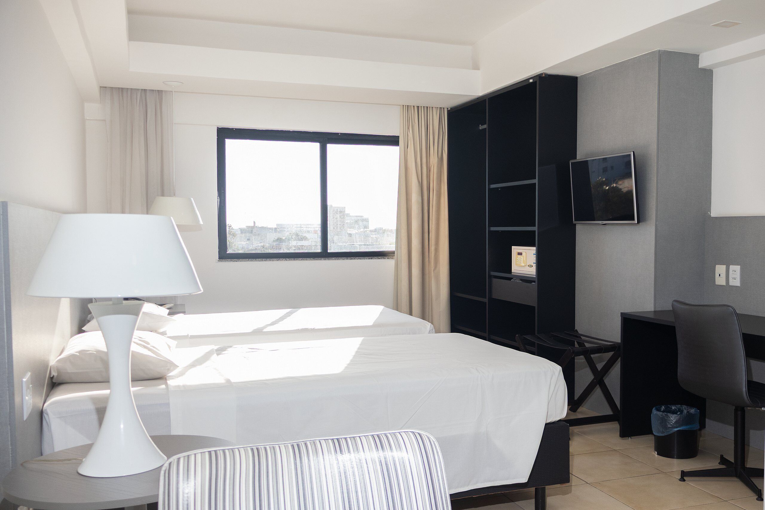 Habitación de hotel con cama, escritorio, silla, televisor y ventana con cortinas.