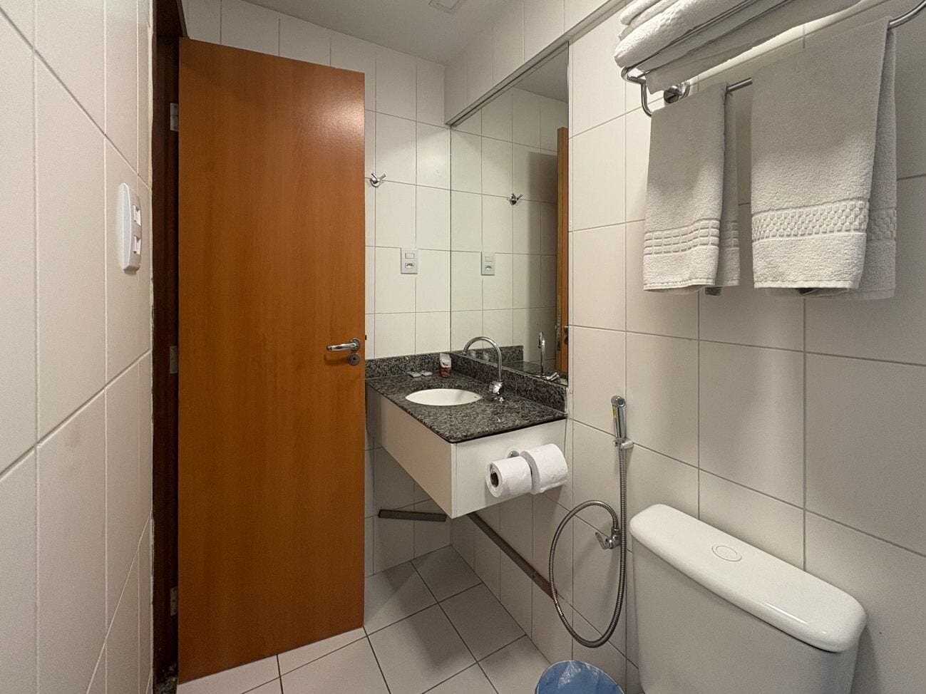 A bathroom with a wooden door, a sink with a granite countertop, a toilet, and a towel rack.