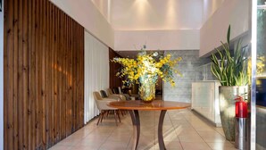 Un interior moderno con una mesa redonda de madera, un jarrón de flores amarillas y una zona de estar con sillas.