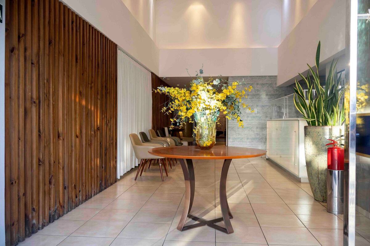 A modern interior with a round wooden table, a vase of yellow flowers, and a seating area with chairs.