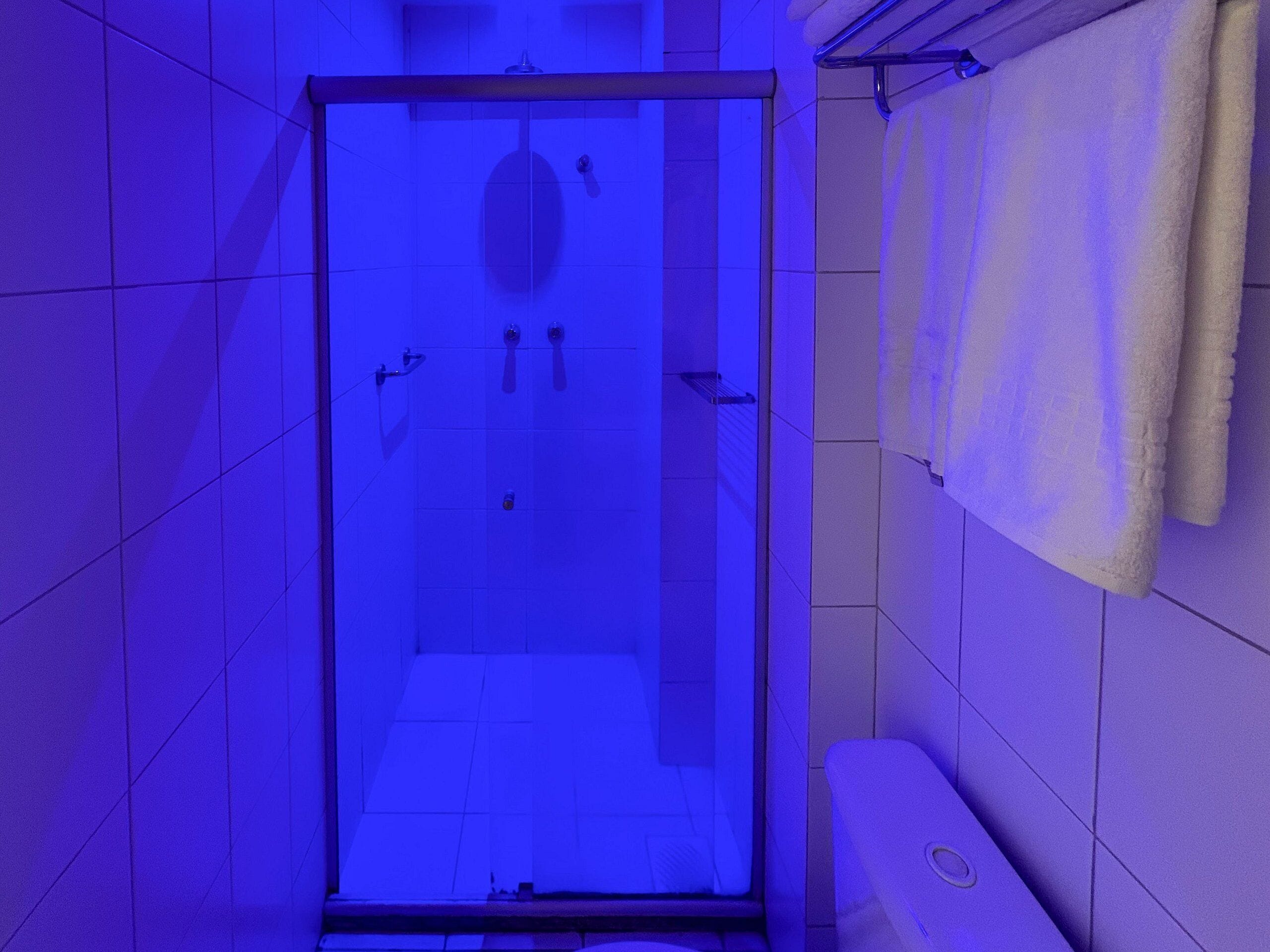 A bathroom with a glass shower enclosure, white tiles, and a towel rack with a white towel.