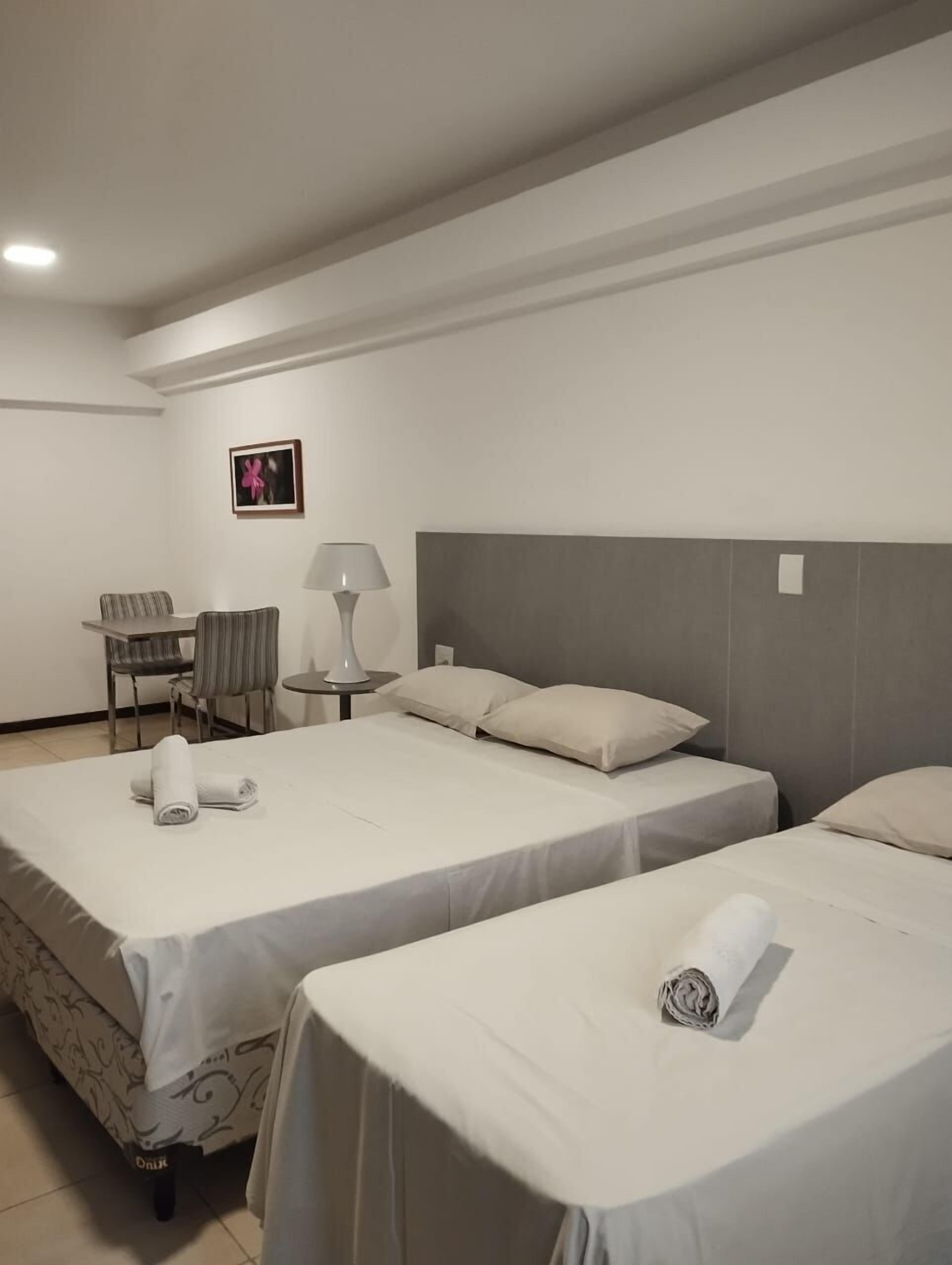 Una habitación de hotel con dos camas, un escritorio, una silla y una lámpara.
