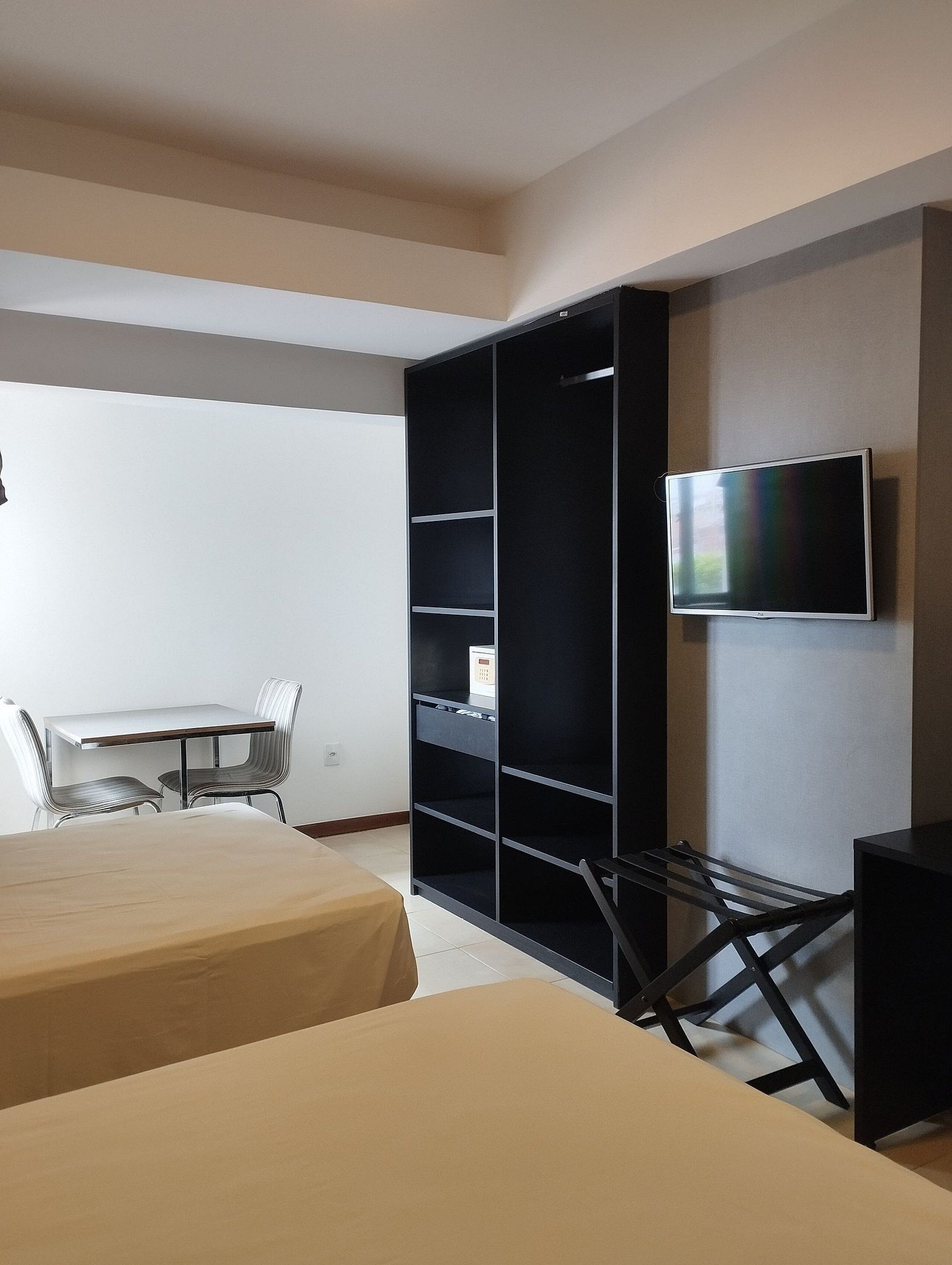Ein Hotelzimmer mit Bett, Schreibtisch, Sessel, Wandfernseher und Kleiderschrank.