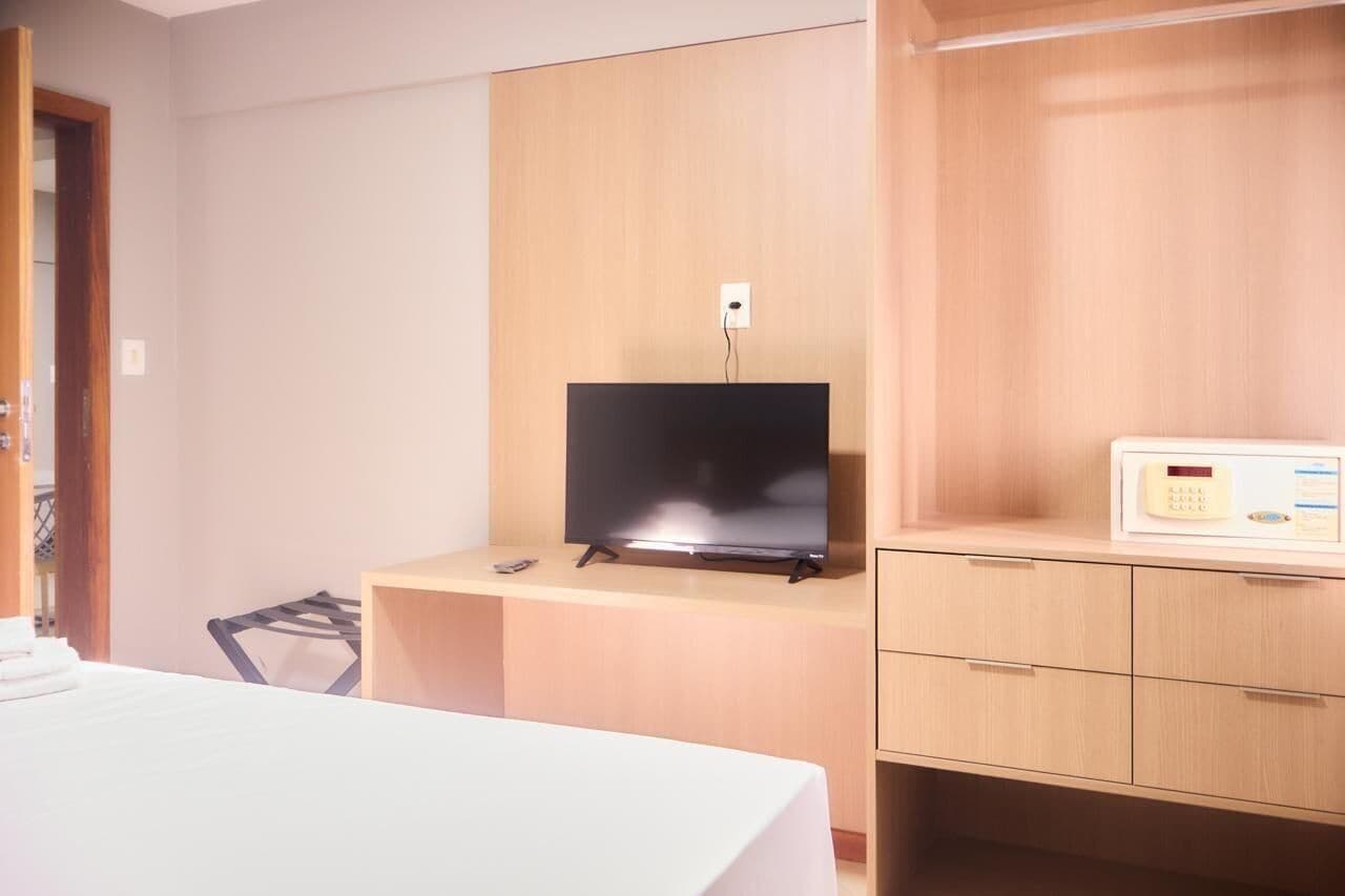 A hotel room with a bed, a desk with a flat-screen TV, a microwave, and a wooden wardrobe.