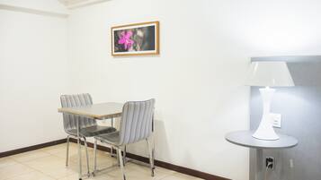 A small dining area with a table and two chairs, a wall-mounted picture, and a lamp on a stand.