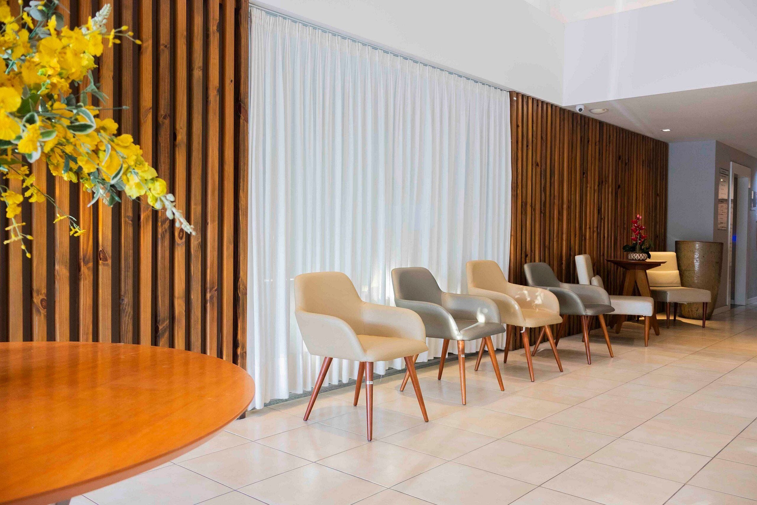 Un moderno vestíbulo de hotel con un panel de madera, una mesa redonda grande y una fila de sillas contemporáneas.