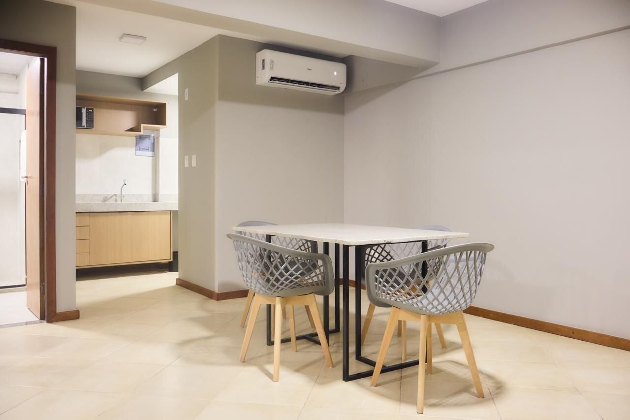 A modern kitchen with a white countertop, wooden cabinets, and a built-in microwave. There is a dining area with a white table and two chairs with a lattice design.