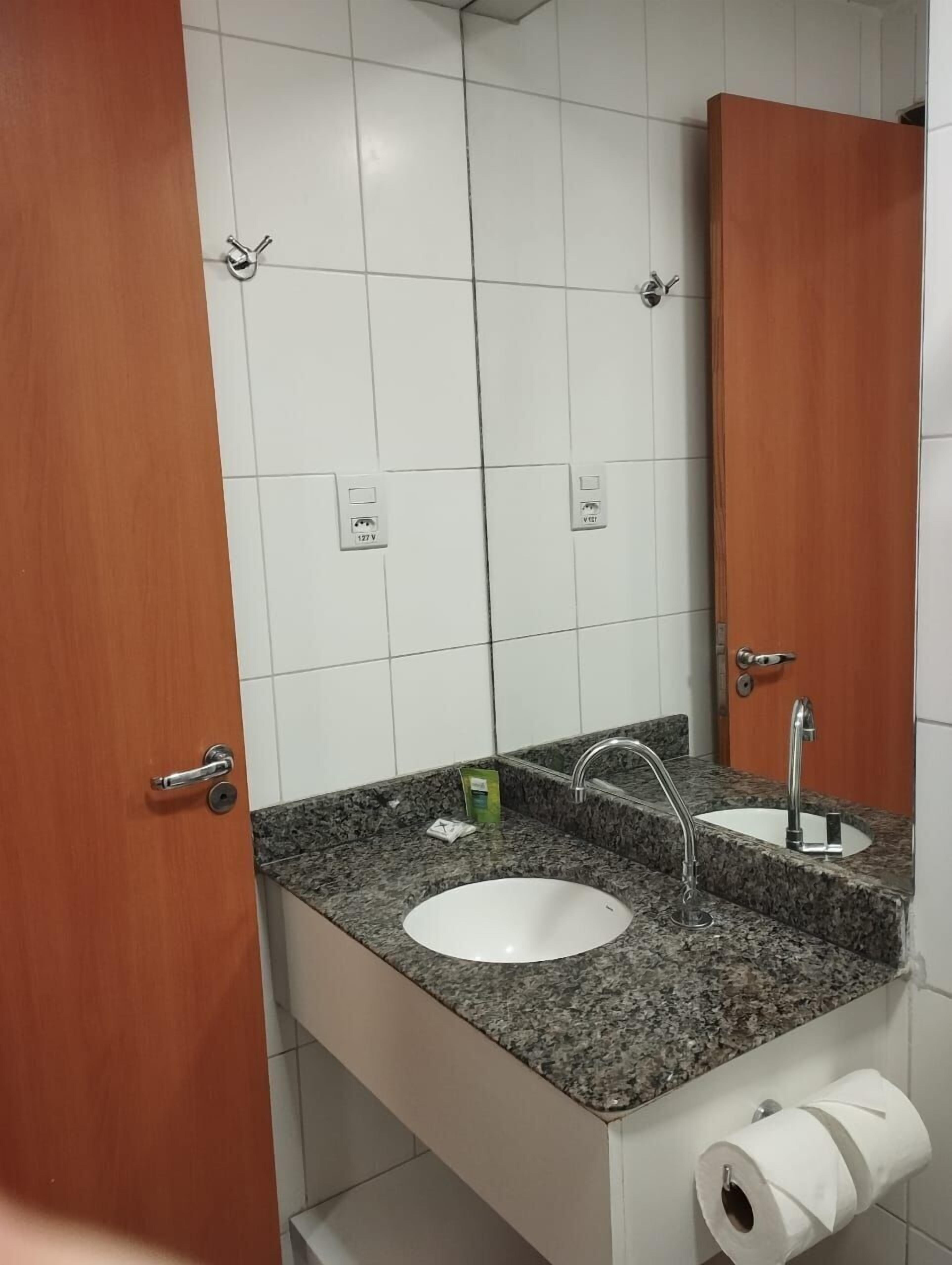A bathroom with two sinks, a mirror, and a toilet paper holder.